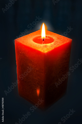 Blurred background with red decorative square red candle burning brightly in darkness of night