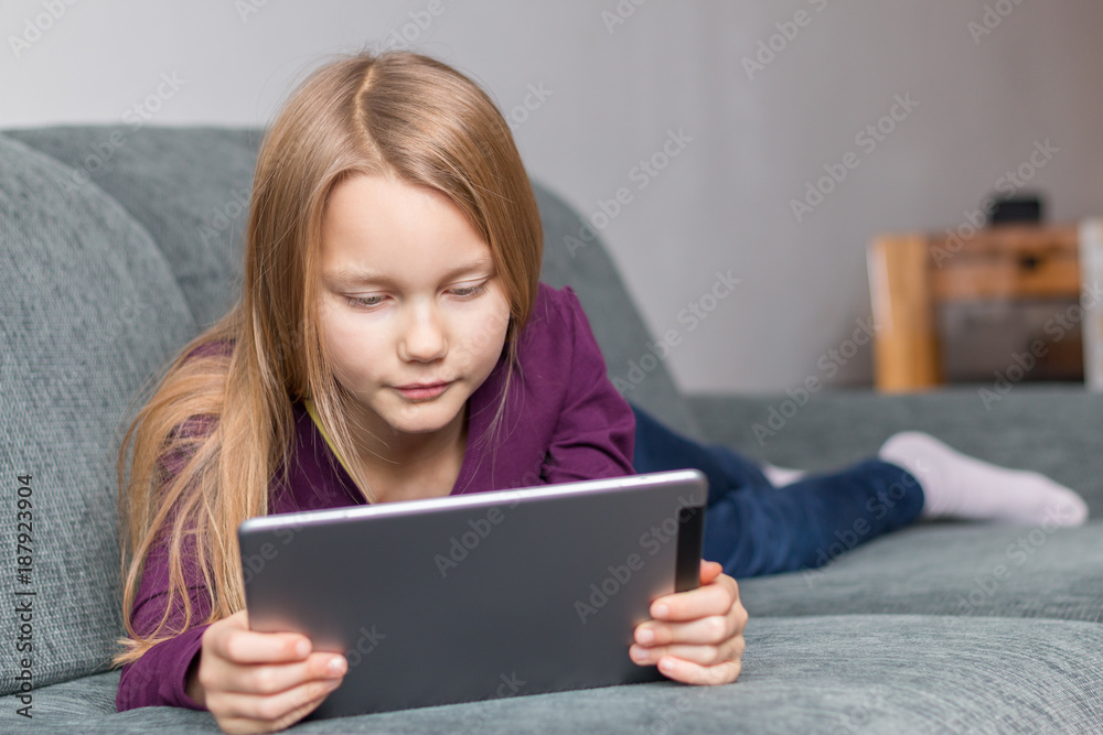 Ein Mädchen liegt mit einem Tablet im Wohnzimmer auf dem Sofa Ein Mädchen liegt mit einem Tablet im Wohnzimmer auf dem Sofa