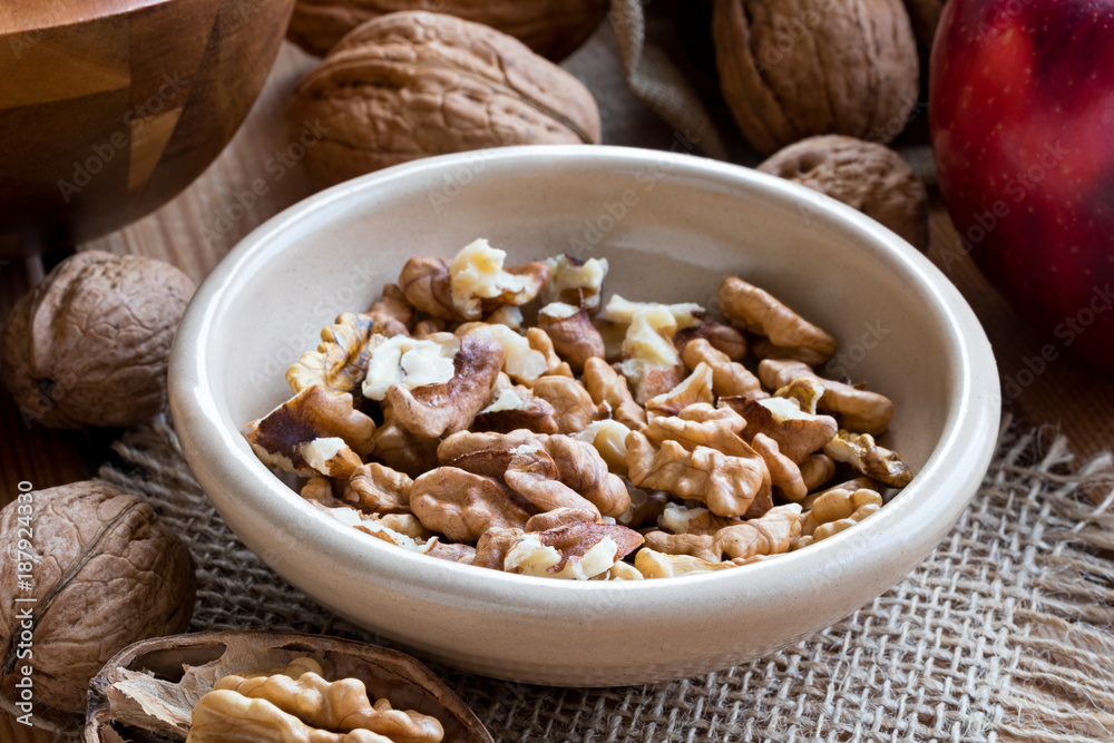Shelled walnuts in a bowl, with whole walnuts in the background Shelled walnuts in a bowl, with whole walnuts in the background