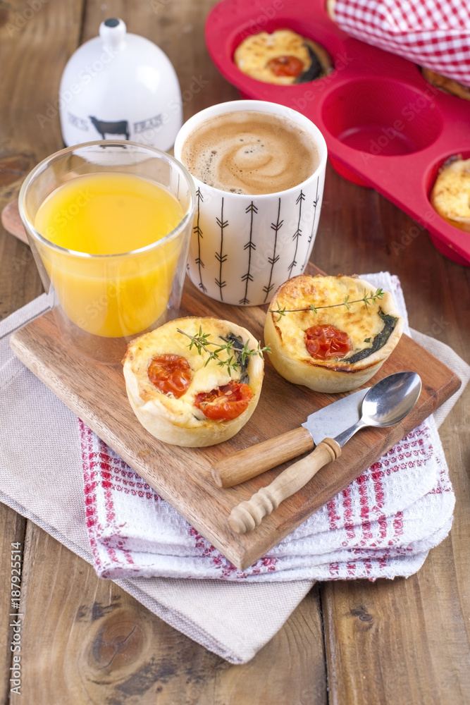 homemade cupcakes with cheese and cherry tomatoes on a wooden board, spoon and knife. table towel in a red cage, a glass of orange juice and fragrant coffee, with space for writing text or advertising