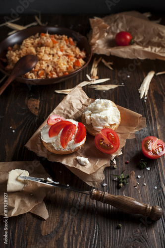 toast with feta cheese on baking paper, cherry tomatoes on the background of pilaf with vegetables and chicken, on a dark wooden table