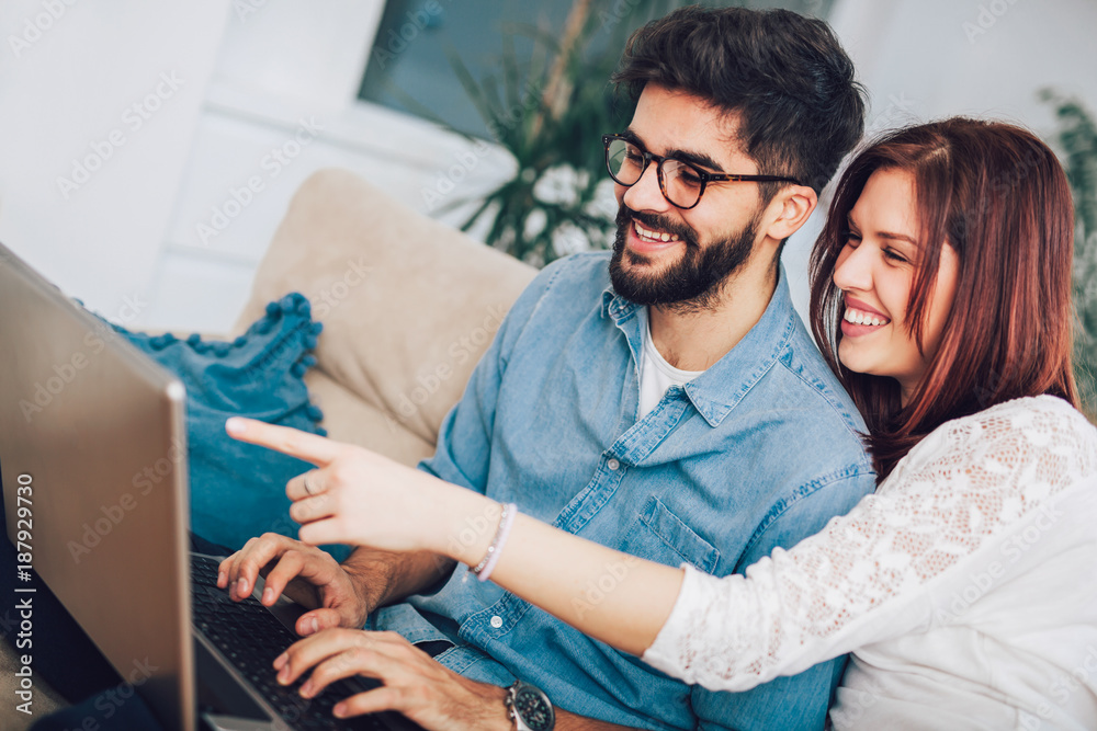 Obraz premium Happy young couple sitting on sofa at home with laptop