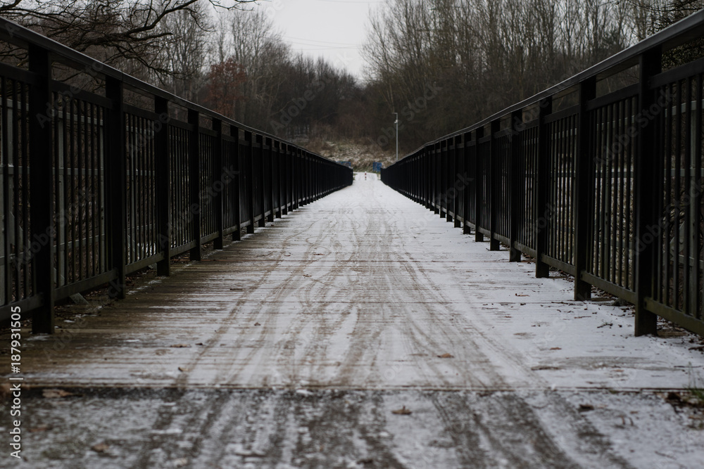 Bridge across the river with black balustrades covered with a thin layer of snow. Narrow bridge with a balustrade.