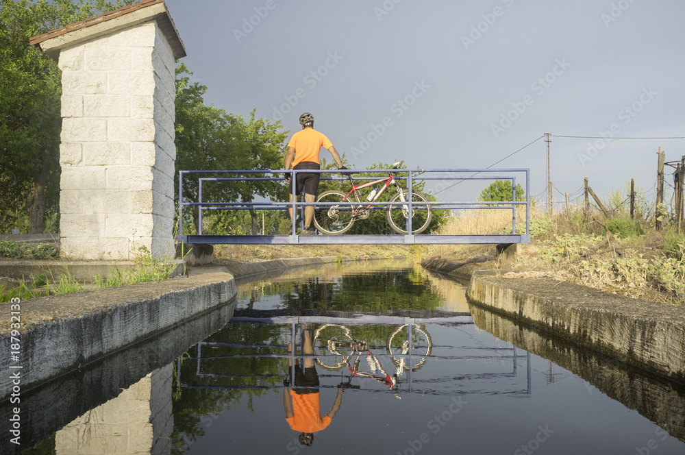 MTB biker crossing a bridge over irrigation canal, Extremadura, Spain