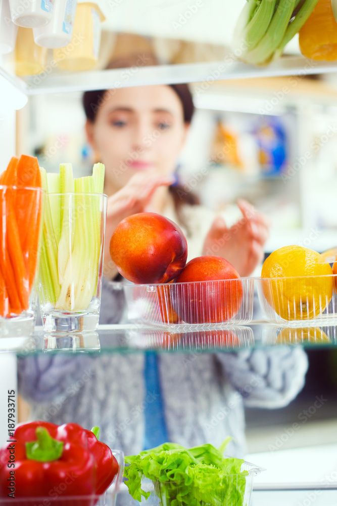 Portrait of female standing near open fridge full of healthy food, vegetables and fruits. Portrait of female