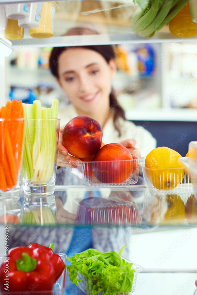 Portrait of female standing near open fridge full of healthy food, vegetables and fruits. Portrait of female