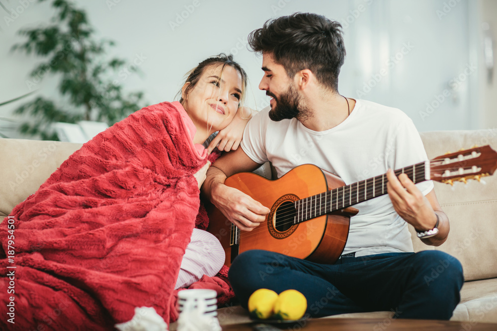 Fototapeta premium Handsome man taking care of his sick girlfriend lying on the sofa