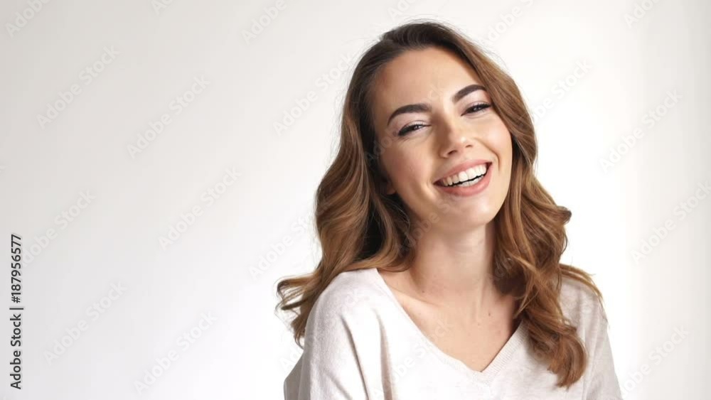Close up view of Pretty smiling brunette woman posing and winks while looking at the camera over grey background Close up view of Pretty smiling brunette woman posing and winks while looking at the camera over grey background