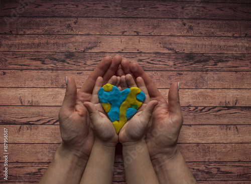 Woman's and child's hands holding a heart of blue and yellow color of world Down syndrome Day.