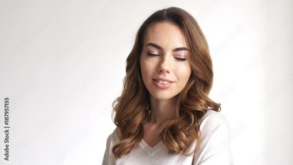 Smiling brunette woman posing and waving at the camera over grey background Smiling brunette woman posing and waving at the camera over grey background