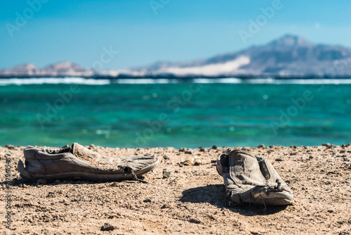 Pair of old shabby shoes on the sandy beach. Old shabby shoes on the sand.