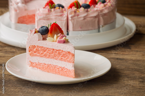 White chocolate strawberry yogurt cake decorated with fresh fruits and chocolate chunk on wood table. Delicious and sweet pink cake for Valentines or birthday party. Homemade bakery concept.