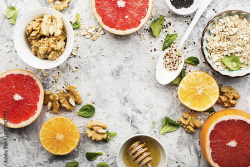 Ingredients of healthy breakfast food  oat flakes  kinoa  walnuts  floral honey  greens  oranges  bloody grapefruits on a light marble background. Top View.
