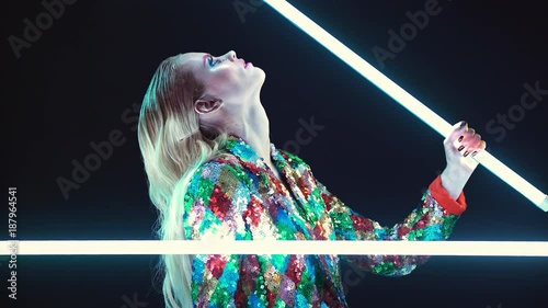 Young blonde woman in an unusual manner playing with led lamps and looking at the camera over black background photo