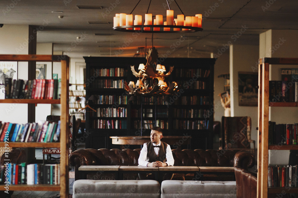Thoughtful man in grey waistcoat poses in the dark library