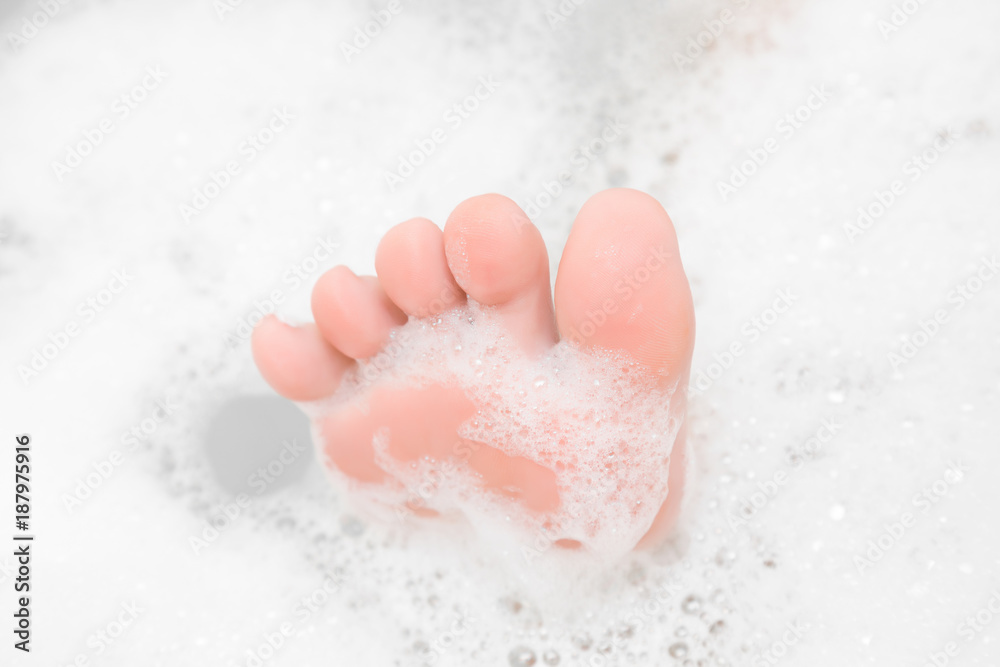Fototapeta premium Funny barefoot. Beautiful groomed woman's foot toes in the bath bubbles. Cares about clean and soft legs skin. Lying and enjoying rest in the bathroom. Relax time. Washing concept.