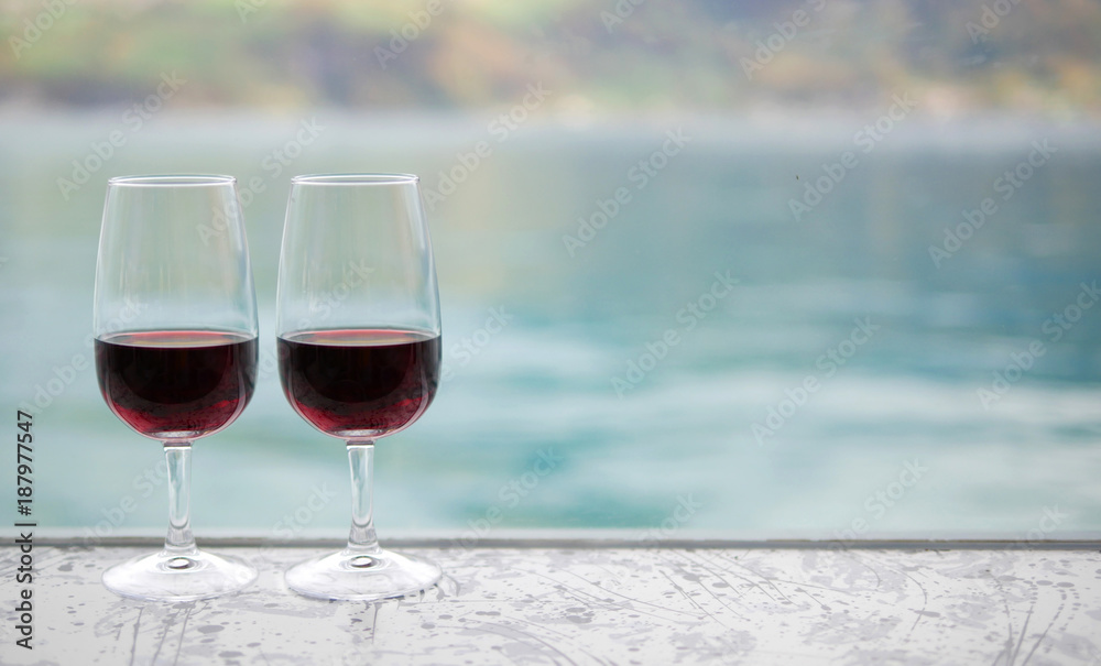 Two red wine glasses on bar over blur green lake background