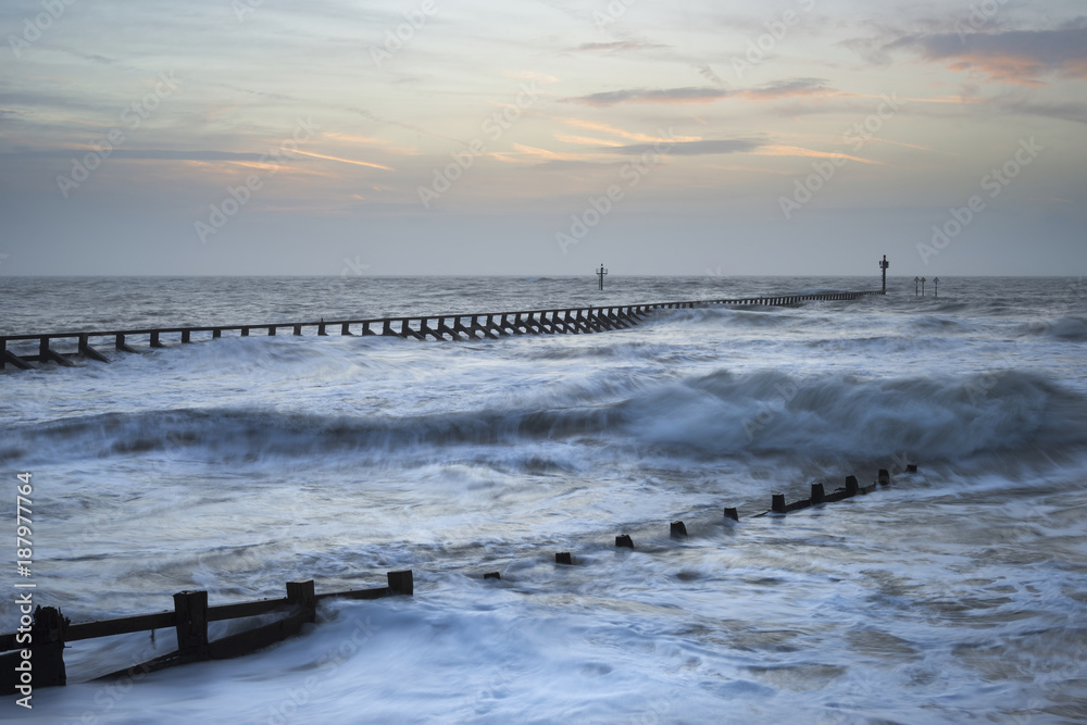 Beautiful dramatic stormy landscape image of waves crashing onto beach at sunrise