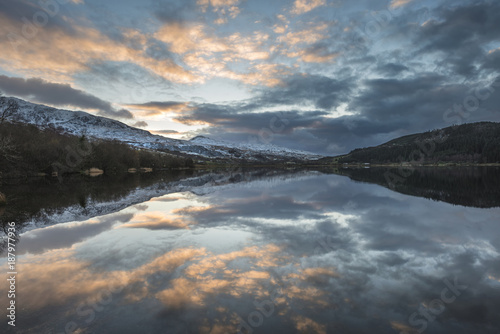 Stunning sunrise landscape image in Winter of Llyn Cwellyn in Snowdonia National Park with snow capped mountains in background