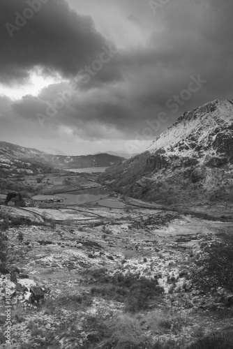 Beautiful black and white Winter landscape image in Llyn Gwynant in Snowdonia National Park with snow capped mountains in background