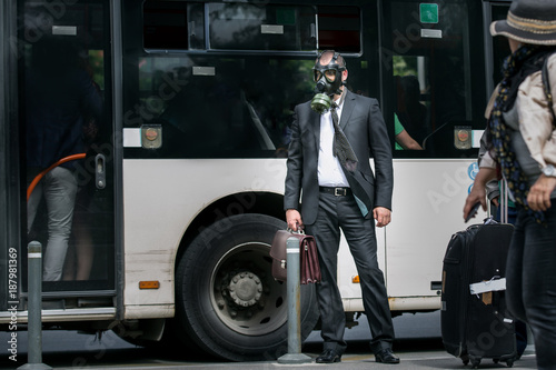 Businessman in a bus station wearing a gas mask on the face.