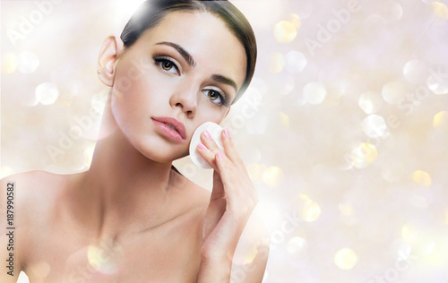 Beautiful woman cleaning her face with cotton pads. Photo of young woman on shiny golden background. Skin care and beauty concept.