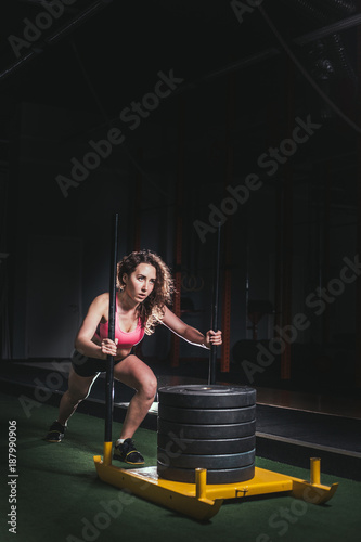 Muscular and strong young female pushing sled on grass turf. Fit woman exercising at cross fit gym.