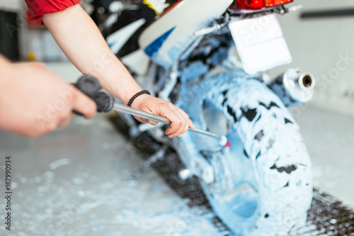 A man cleaning motorcycle with sponge using blue foam, car detailing (or valeting) concept. Selective focus. 