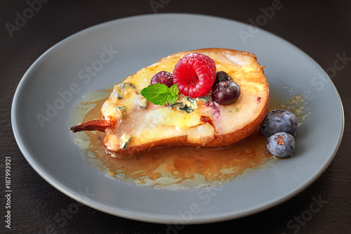 Closeup on half baked pear with blue cheese and berries on dark