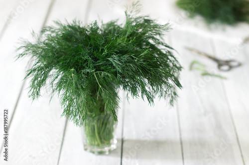 Fresh dill in a glass on a white wooden background. Rustic style, selective focus.