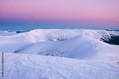 Wonderful sunrise in the Carpathians in winter. Snow-covered summits of winter mountains in the red rays of sunrise. Fresh footprints in the snow on top of the mountain.