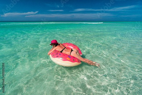Smiling beautiful brunette woman in pink hat is swimming on a big inflatable tube at the coast of Caribbean Sea