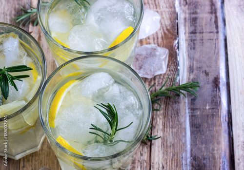 Cold lemon drink with rosemary, ice and tonic, on rustic wooden table. Selective focus