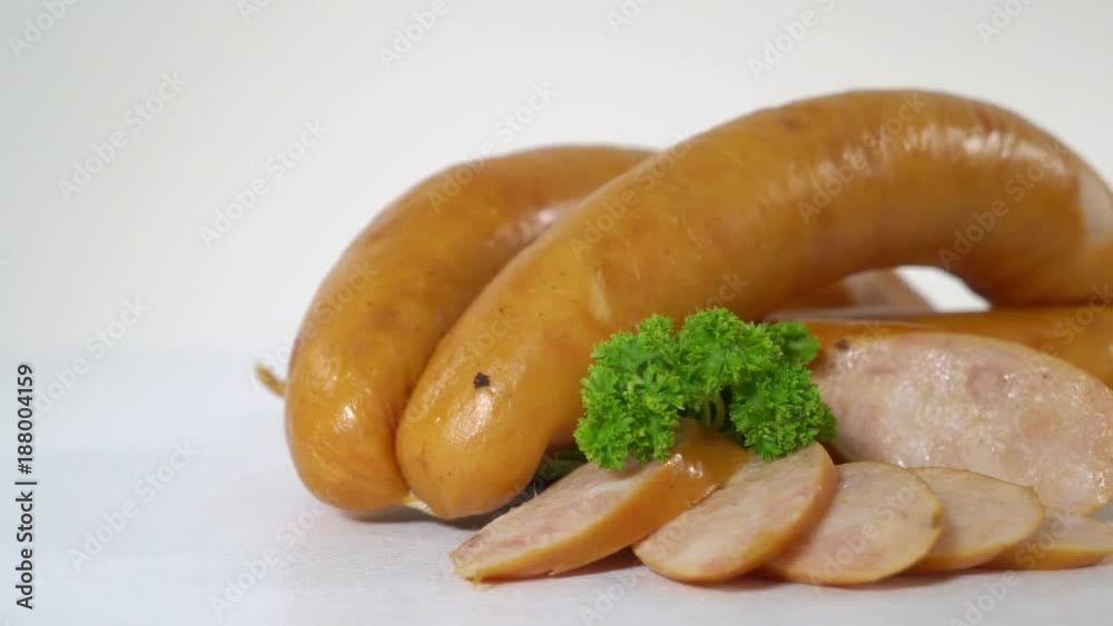 Processed meat products sliced. Sausage cut with slices and herbs on white background. Sausages in a natural casing. Closeup, dolly shot.
