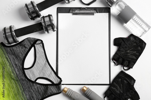 Clipboard with blank paper for exercise plan and gym stuff on white background. Flat lay composition