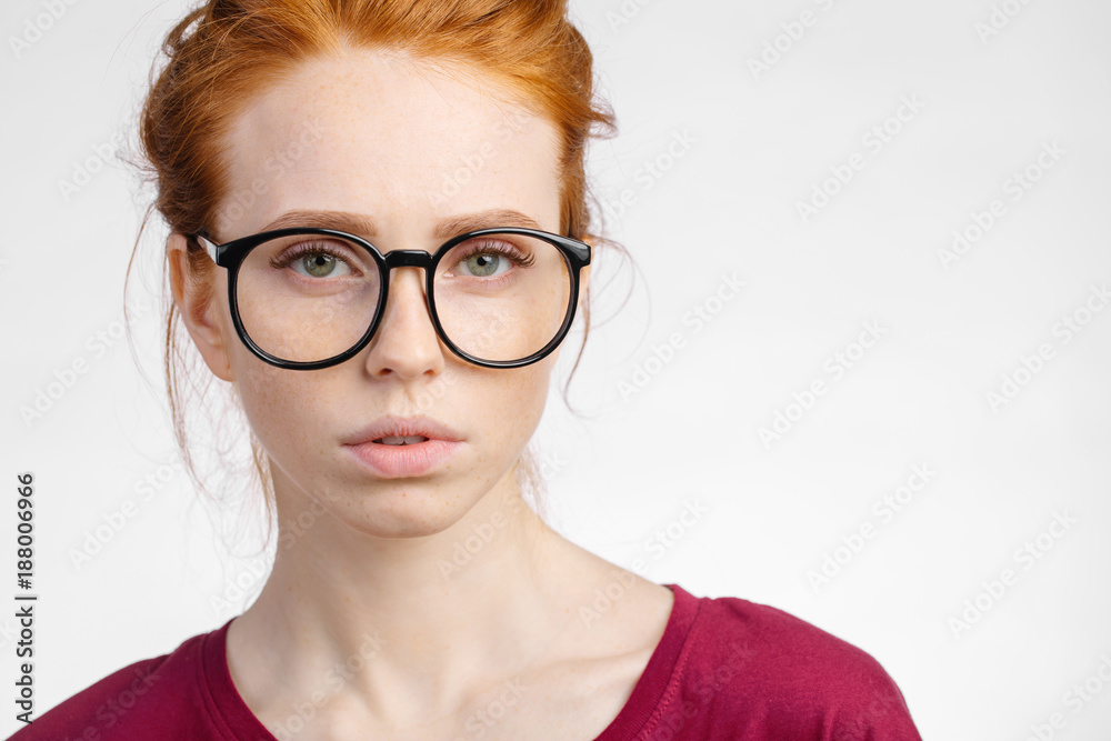 close up young redhead woman in glasses with hair knot looking at camera on white background close up young redhead woman in glasses with hair knot looking at camera on white background
