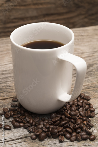 coffee in large white mug surrounded by roasted coffee beans shot against rustic brown barn wood background
