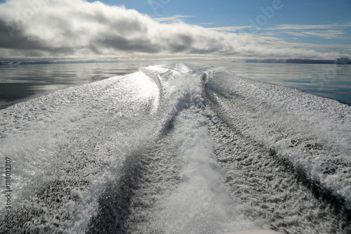 Waves behind speed boat under a light made by sun and clouds