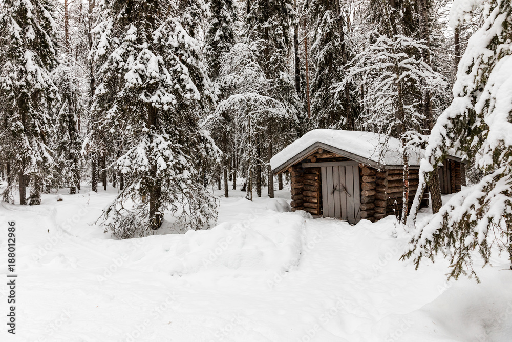 a wooden house in the snow-covered forest near The Raudanjoki river, Rovaniemi, Finland.