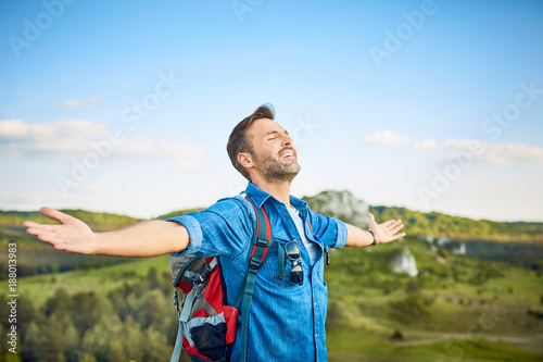 Cheerful man extending arms and embracing the beauty of the mountains during hiking trip