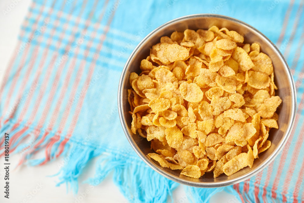 Cornflakes in a metal bowl on a painted white wooden background. Composition with a dish towel.