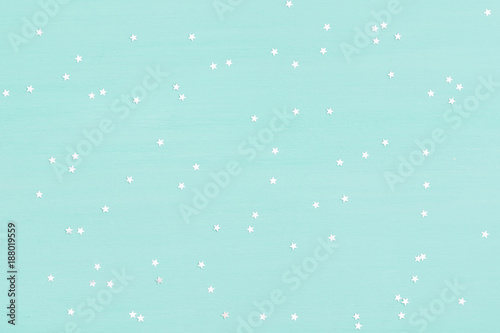 Many small shinny silver stars on turquoise wooden background