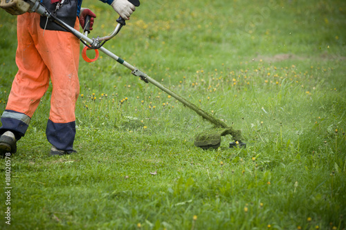 A man with a lawnmower on grassy field in the yard. Man mowing grass with a trimmer.
