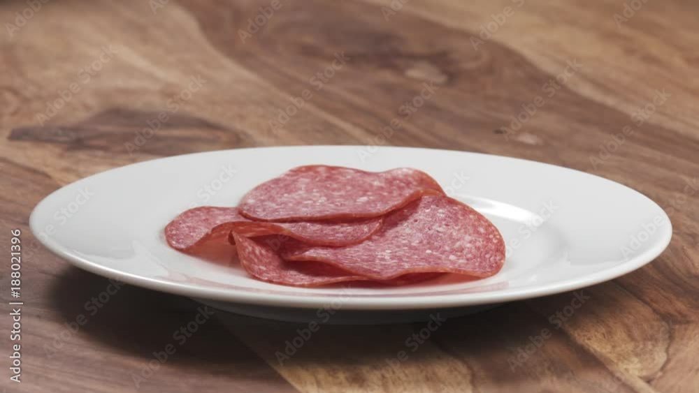 Slow motion closeup thin salami slices falling on white plate Slow motion closeup thin salami slices falling on white plate