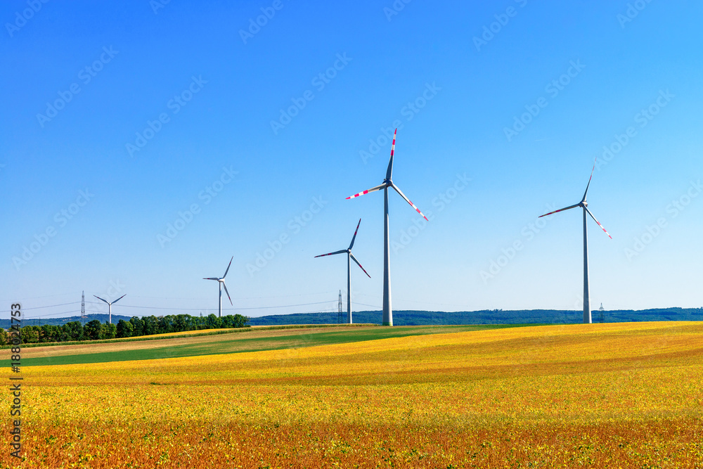 White wind power plants in a field at summer sunset light White wind power plants in a field at summer sunset light