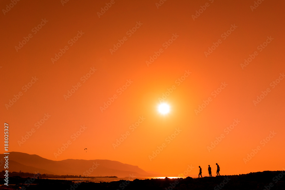 Silhouette einer Gruppe von Menschen vor Meer bei Sonnenuntergang.