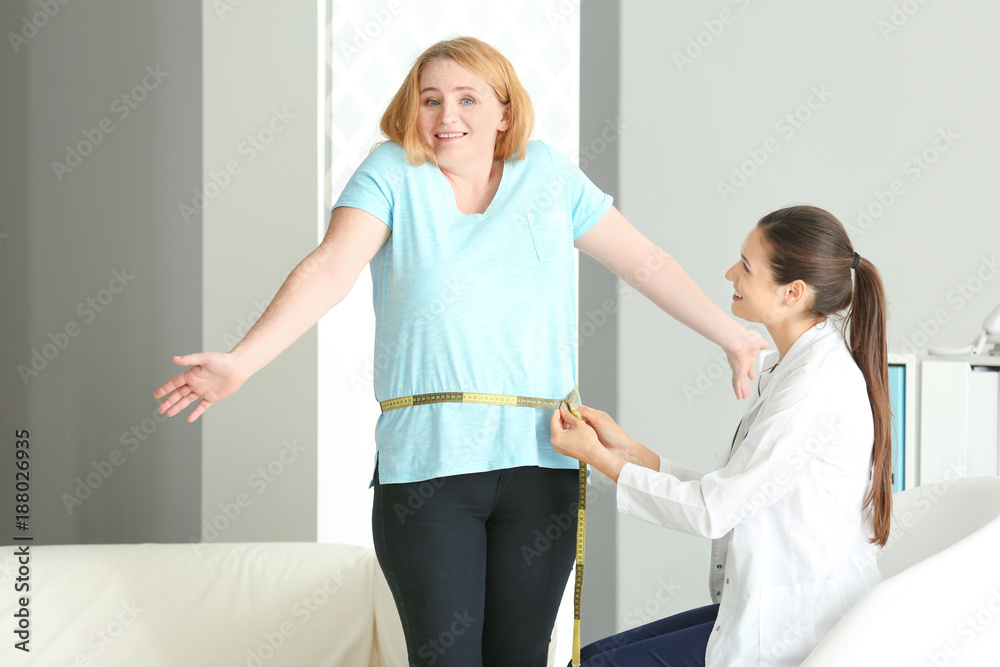 Young female doctor measuring waist of overweight woman with centimeter in clinic Young female doctor measuring waist of overweight woman with centimeter in clinic