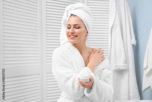 Young woman in towel and bathrobe using cosmetic product at home