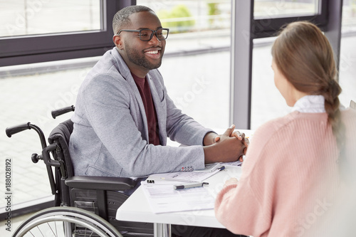 Handsome cheerful black male invalid in wheelchair involved in charity, meets with female investor, discuss main details, helps physically challenged people. People, health and business concept