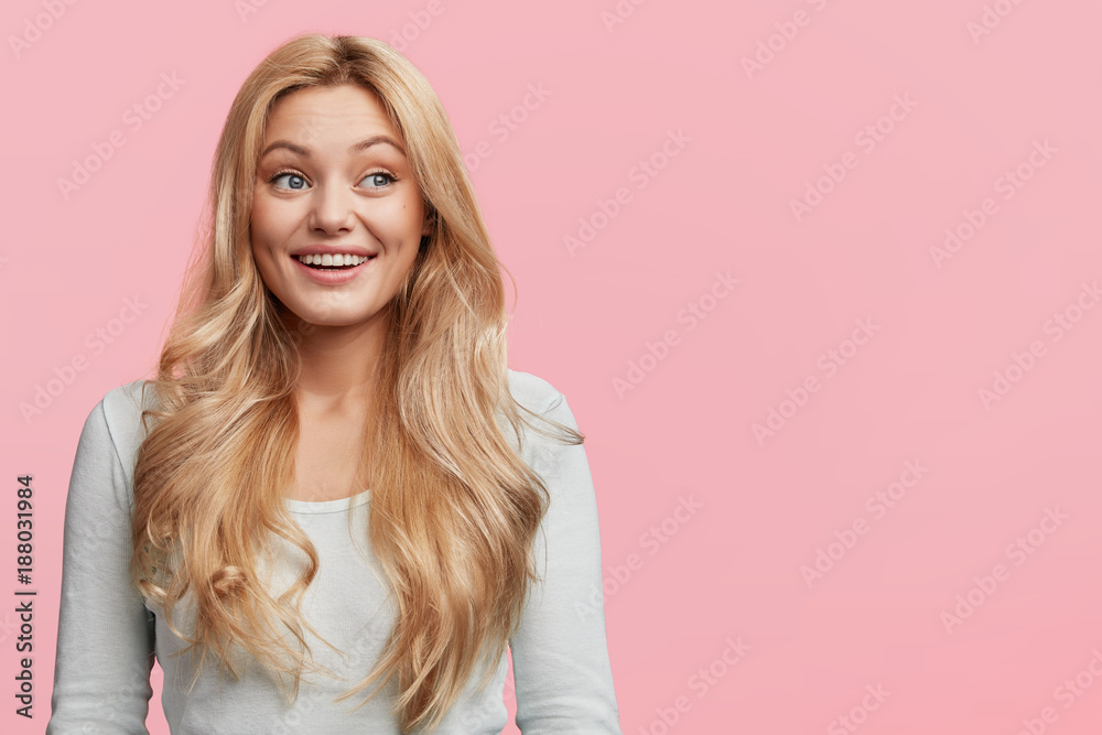 Photo of pleasant looking blonde female with long straight hair, being in good mood after dating with handsome boyfriend, dreams about wedding and creating own family, isolated over pink wall Photo of pleasant looking blonde female with long straight hair, being in good mood after dating with handsome boyfriend, dreams about wedding and creating own family, isolated over pink wall